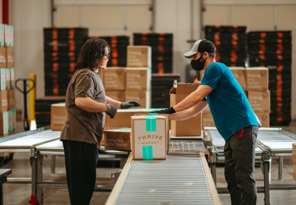 Two Thrive Market fulfillment center employees prepare a box for shipment. 