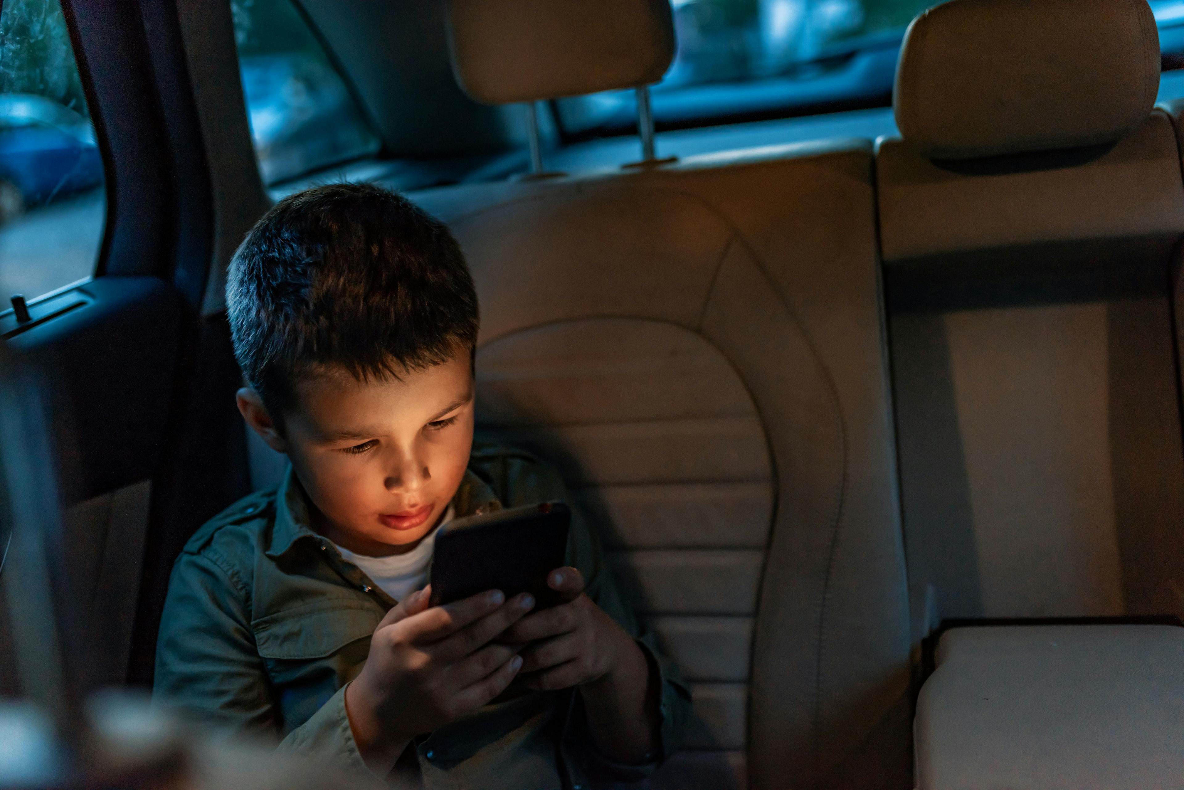 A child in a car looks at a smartphone. 