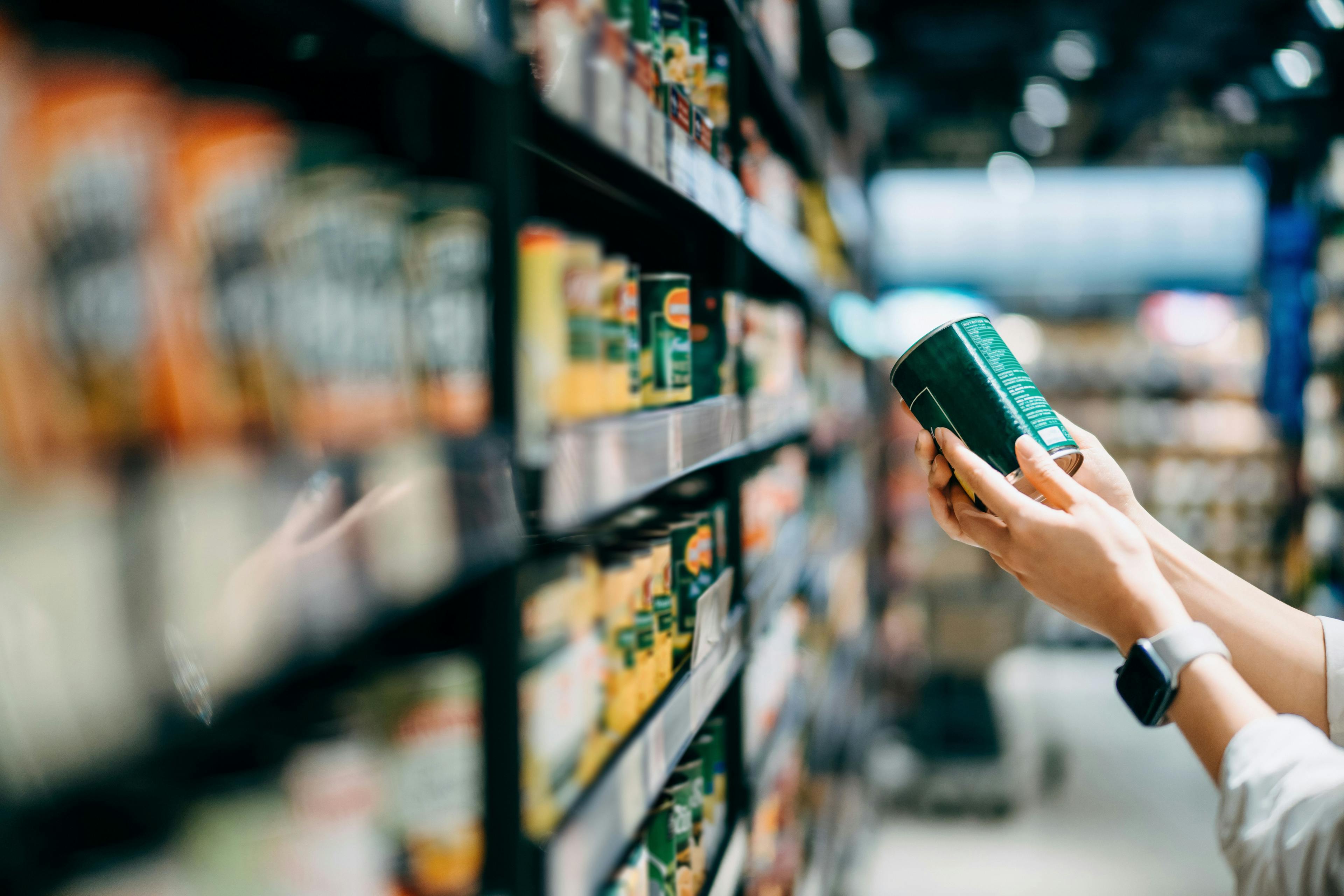 Hands of person checking the label on a can in a grocery store aisle