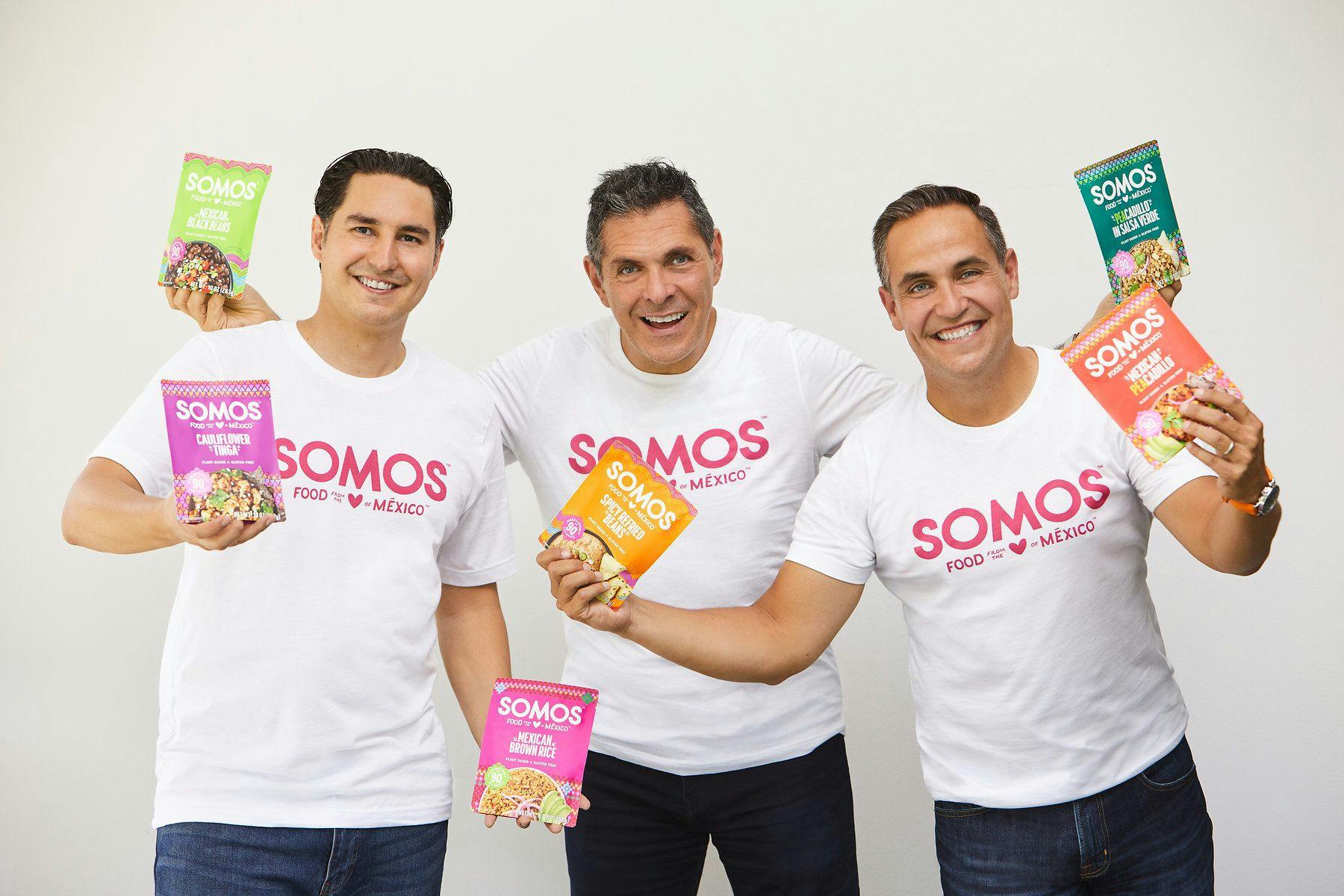 Three men wearing branded T-shirts holding up Somos products