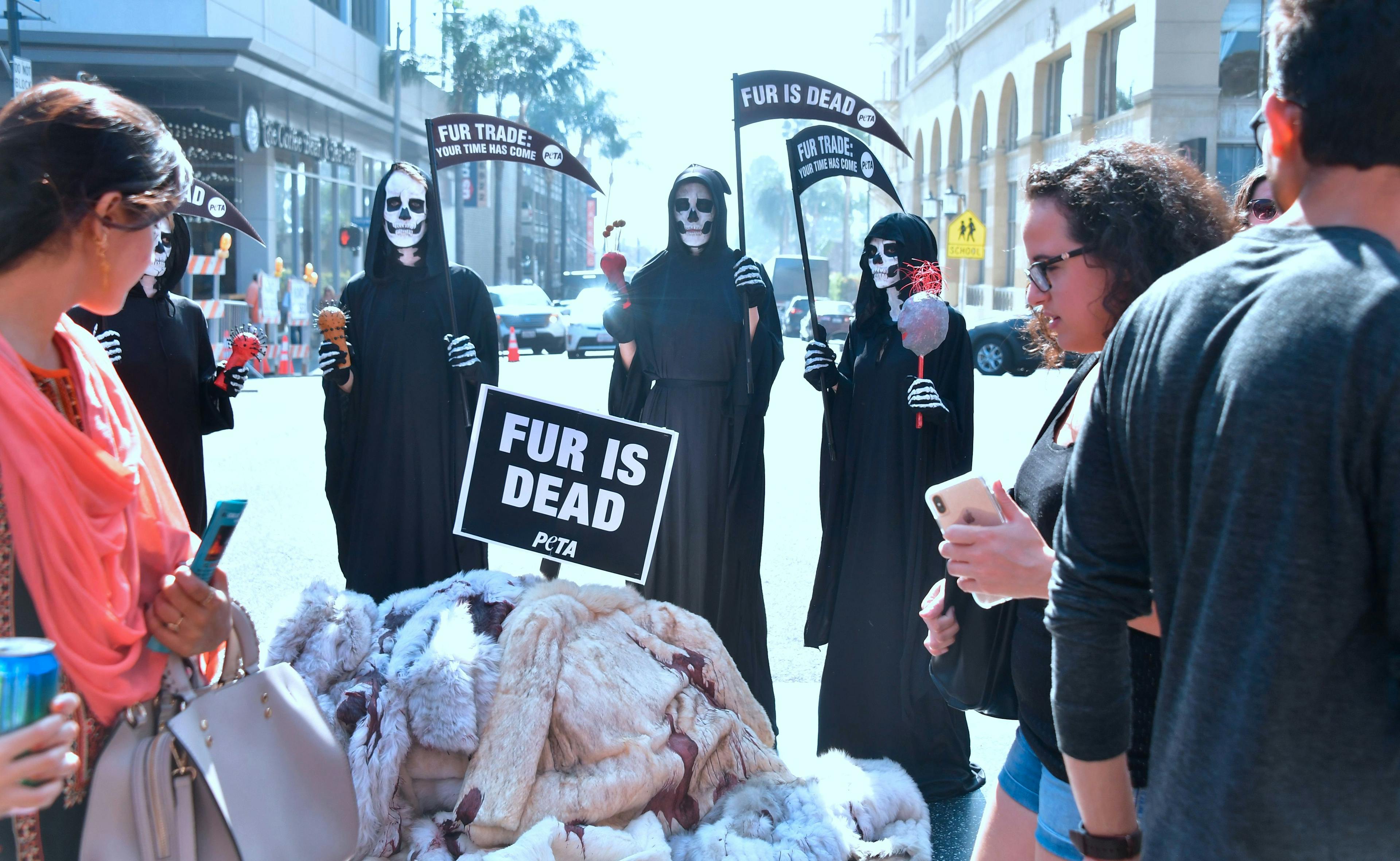 Pedestrians walk past PETA activists dressed as Grim Reapers holding a "Fur is Dead" rally